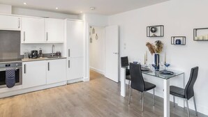A modern kitchen with white cabinets, a dining area with a glass table, and a ceiling light fixture. - Bright 1-Bedroom Apartment with Free Parking (London)