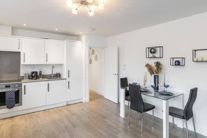 Une cuisine moderne avec des meubles blancs, un coin repas doté d’une table en verre et un luminaire au plafond.