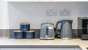 A kitchen counter with a coffee maker, a kettle, and labeled containers for tea and sugar. - Bright 1-Bedroom Apartment with Free Parking (London)