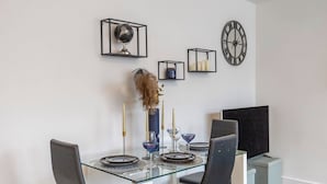 A modern dining area with a glass table, black chairs, and decorative wall art including a globe and clocks. - Bright 1-Bedroom Apartment with Free Parking (London)