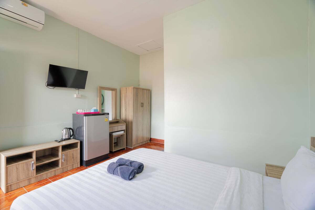 A hotel room with a bed, a TV, a minibar, and a wooden wardrobe.