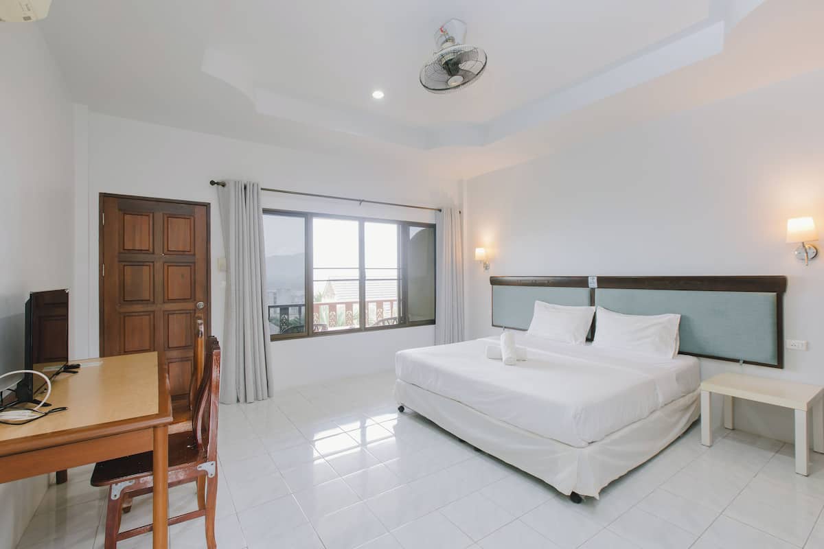 A hotel room with a bed, bedside table, desk, chair, and a window with curtains.