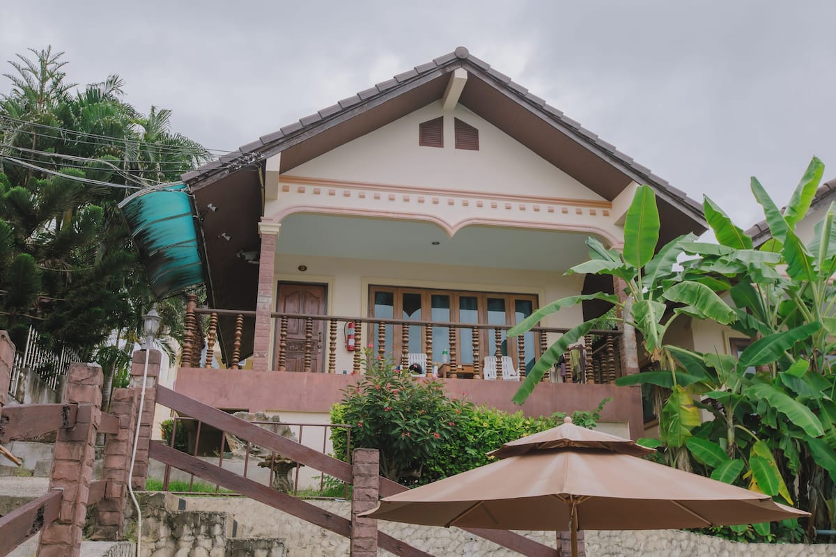 A two-story house with a balcony, a staircase, and a large umbrella.