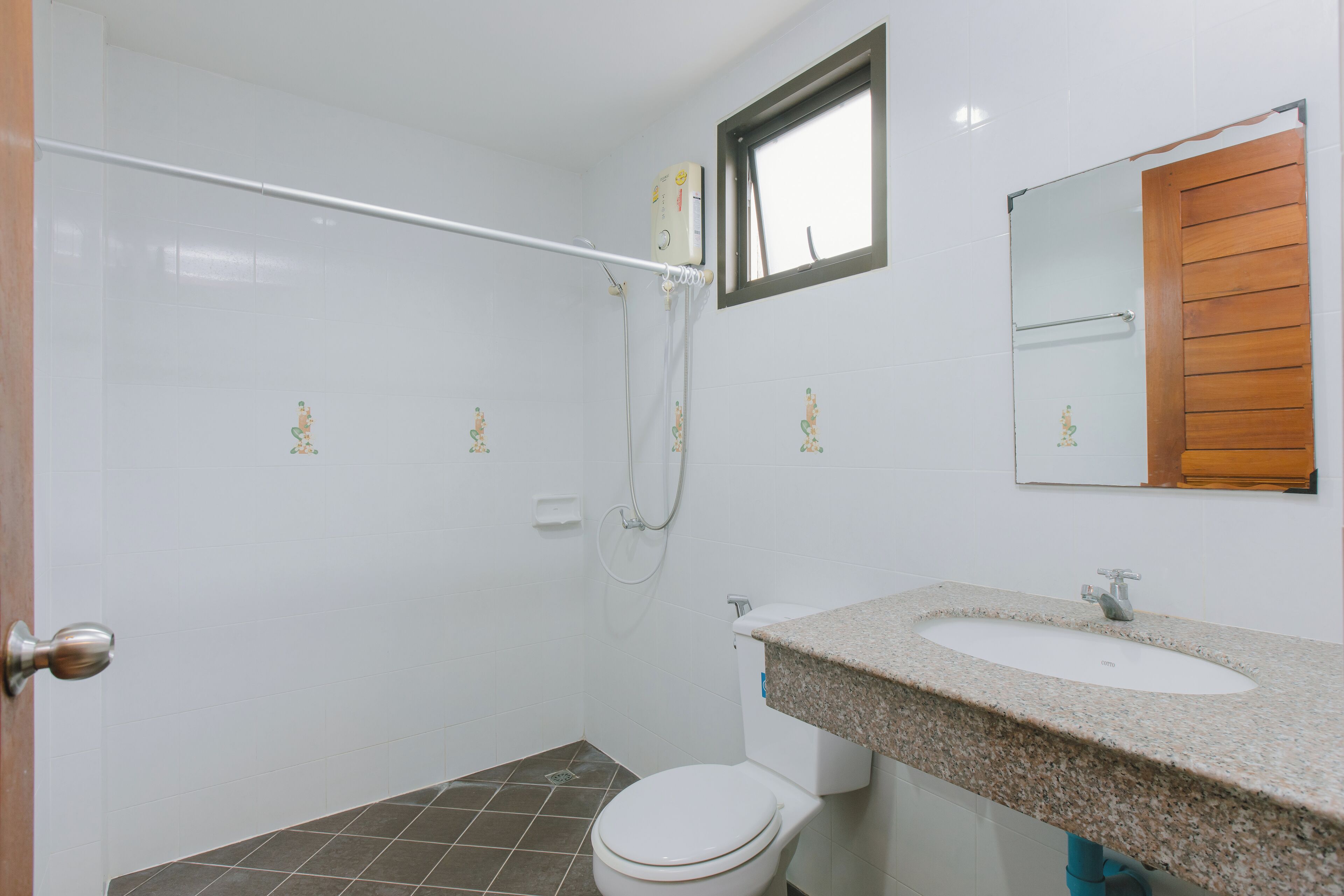 A bathroom with a white toilet, a sink with a granite countertop, a shower with a glass door, and a wooden door.