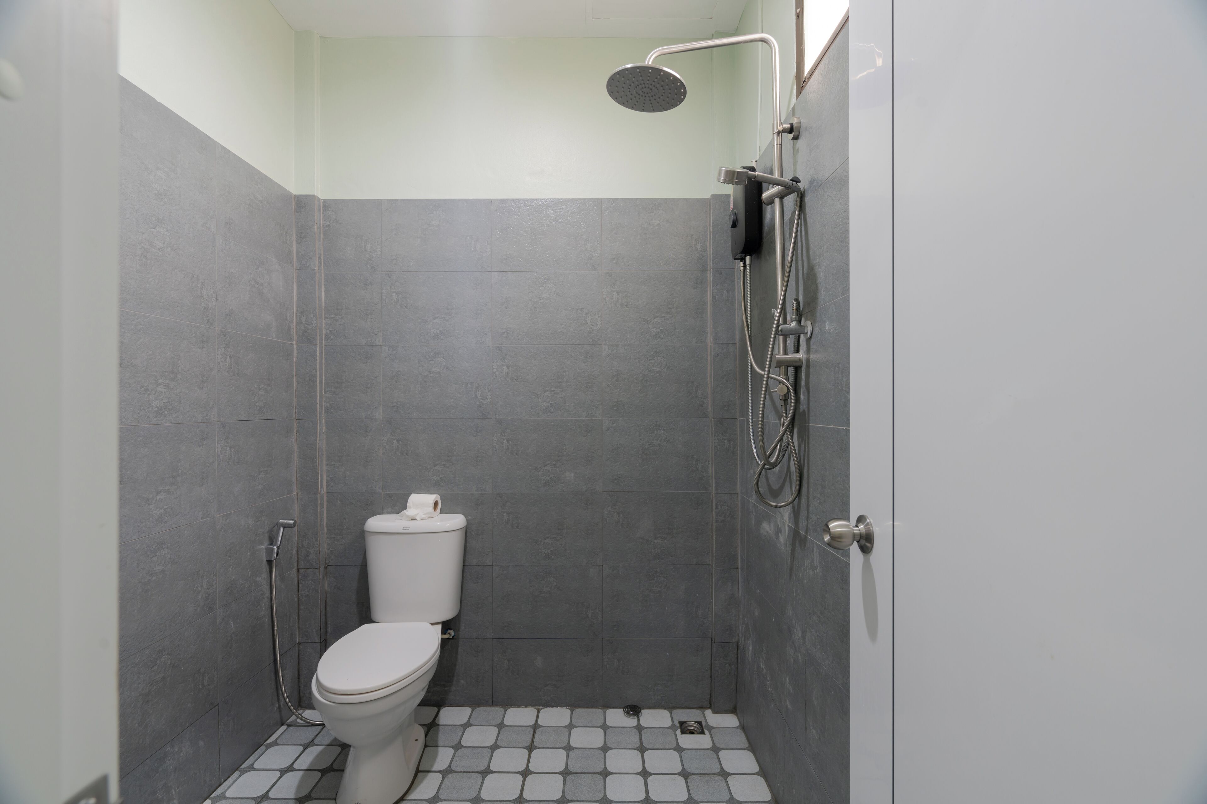 A small, modern bathroom with a toilet, shower, and tiled floor.