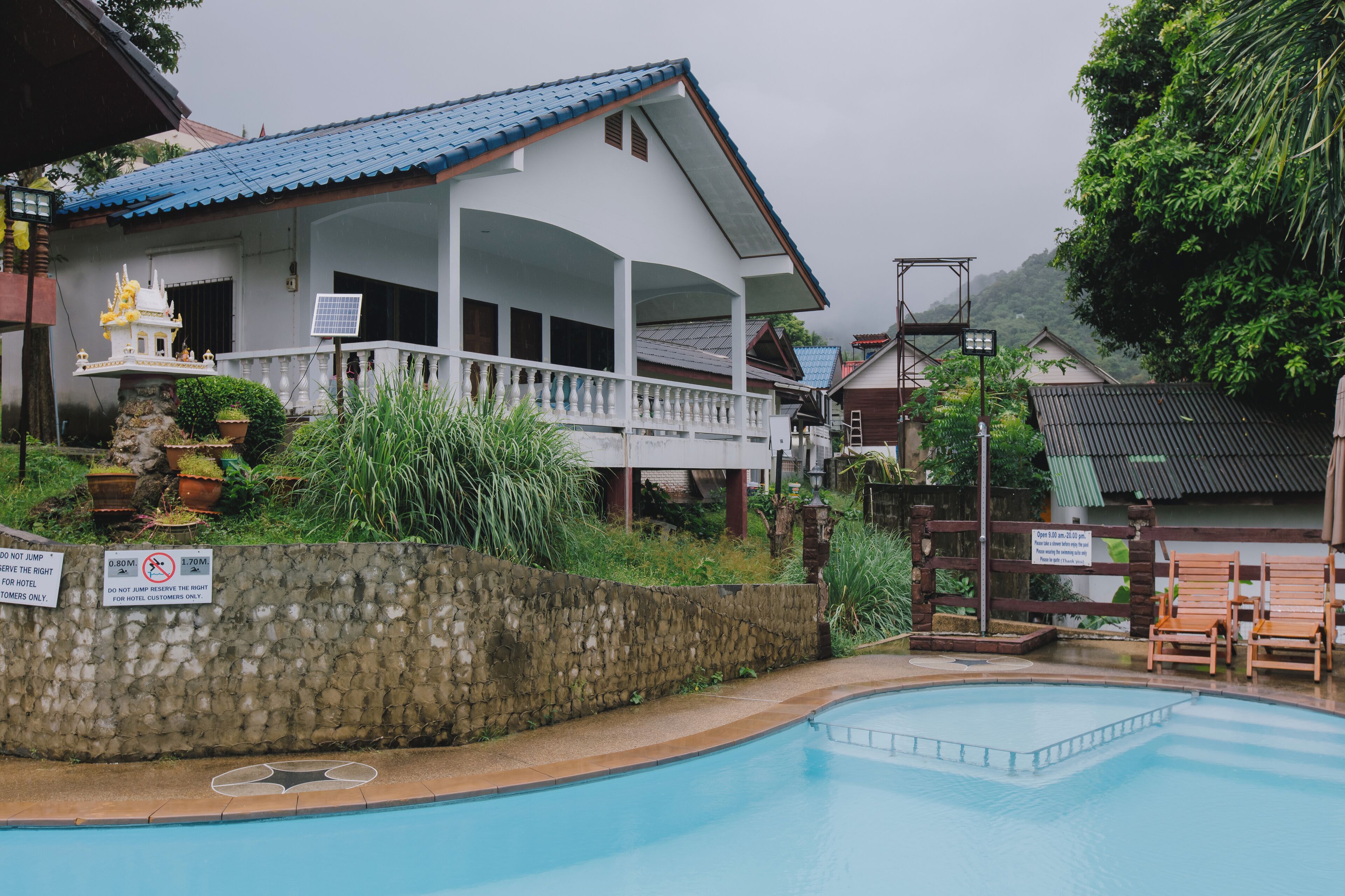 Un hotel con piscina, una zona techada con una estatua, y señalización que indica áreas para huéspedes.