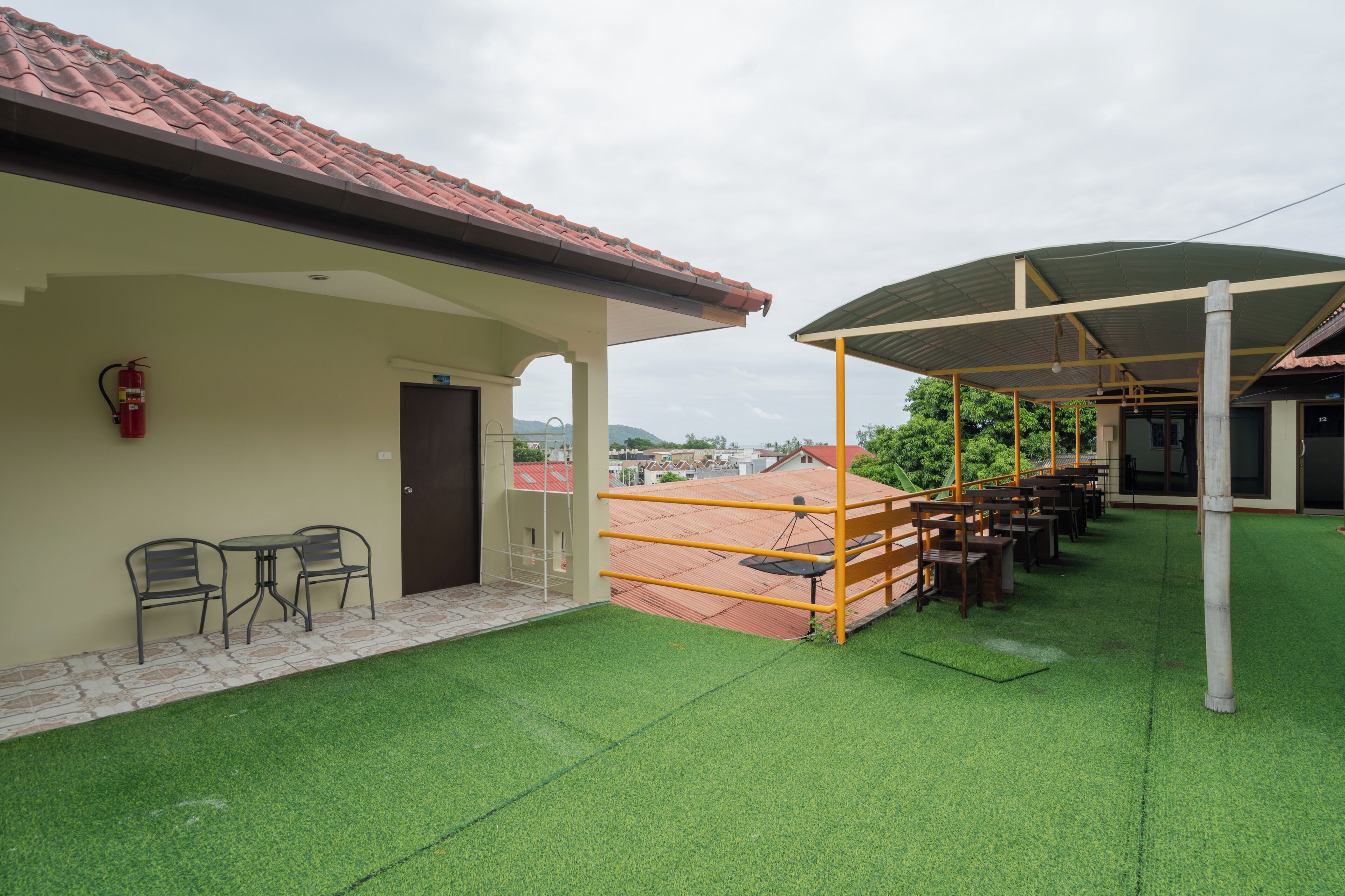 A covered outdoor seating area with artificial grass, a fire extinguisher, and a view of the surrounding buildings.