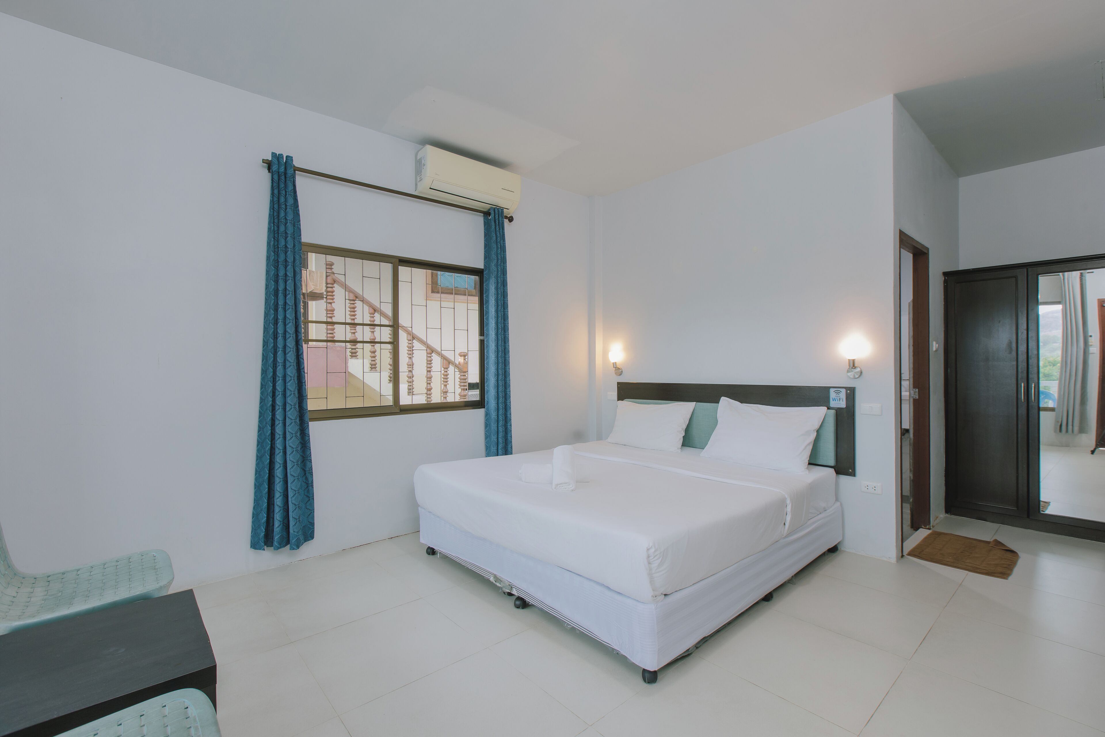 A bedroom with a single bed, a window with curtains, an air conditioning unit, and a door leading to another room.