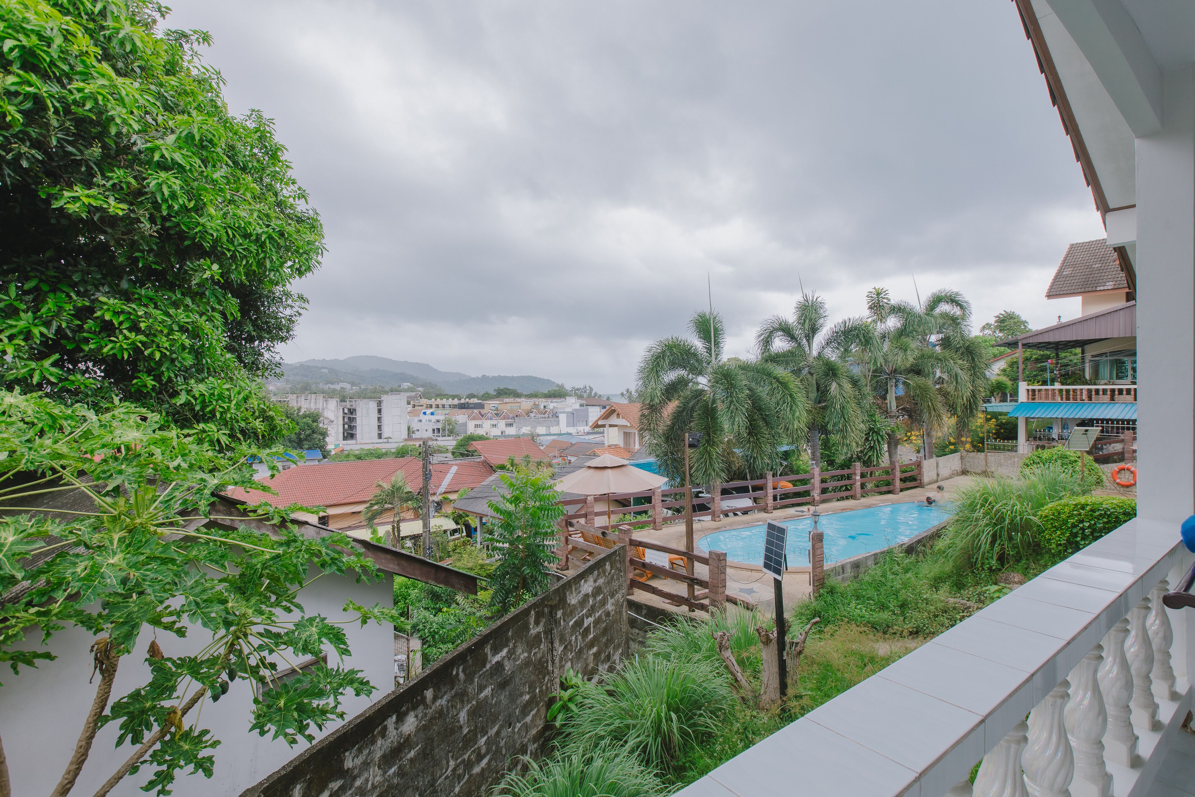 A view of a swimming pool surrounded by greenery and buildings, with a cloudy sky above.