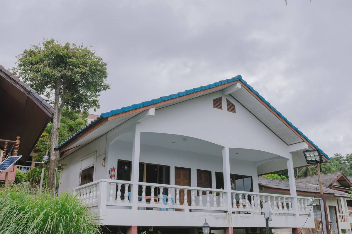 A two-story house with a balcony, a solar panel, and a blue roof.