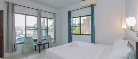A hotel room with a bed, a chair, a table, and large windows offering a view of the city.