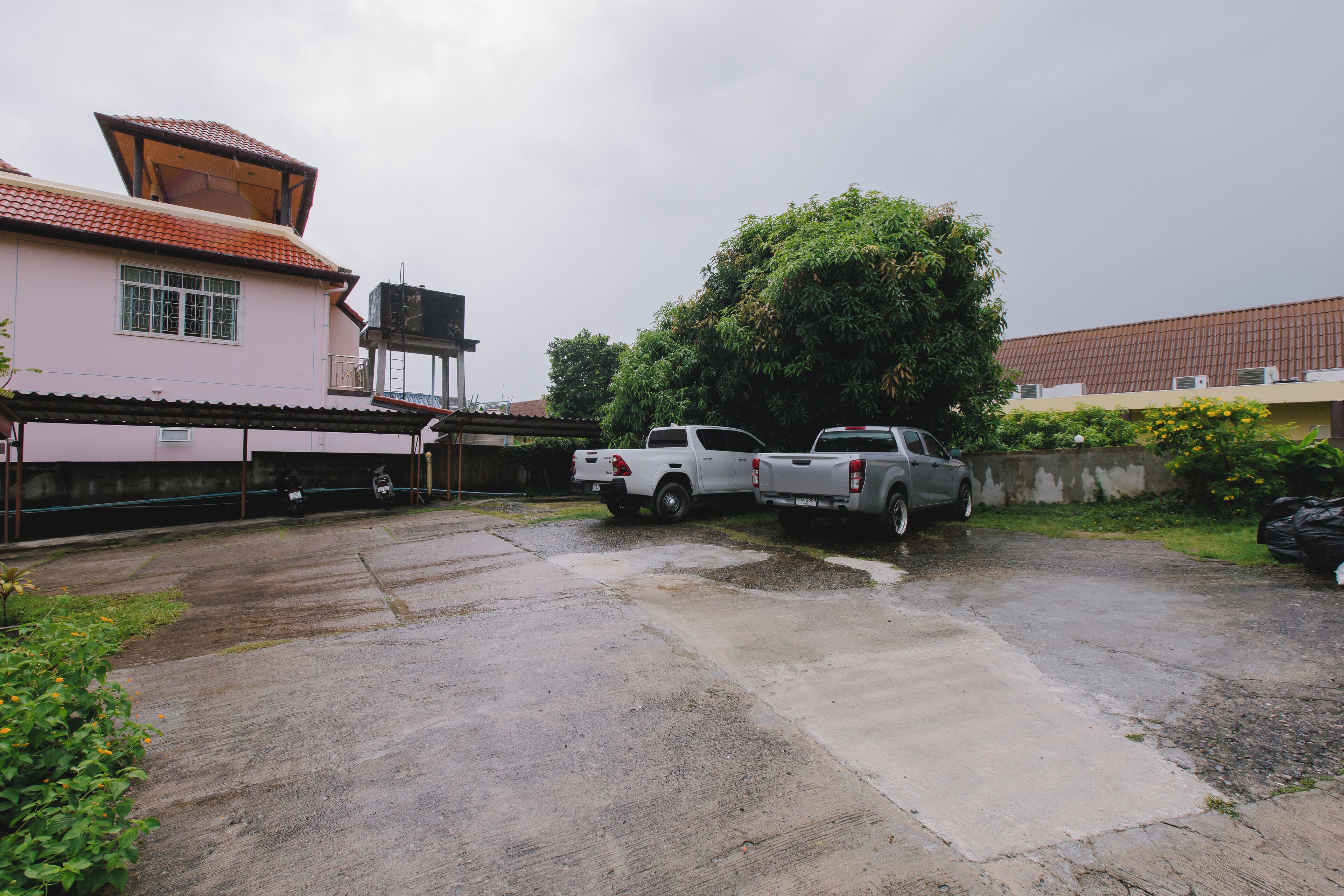 A residential area with a pink house, a white pickup truck, and a grey pickup truck parked in the driveway.