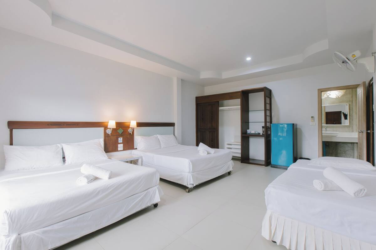 A hotel room with two single beds, a wardrobe, a minibar, and a bathroom with a mirror and sink.