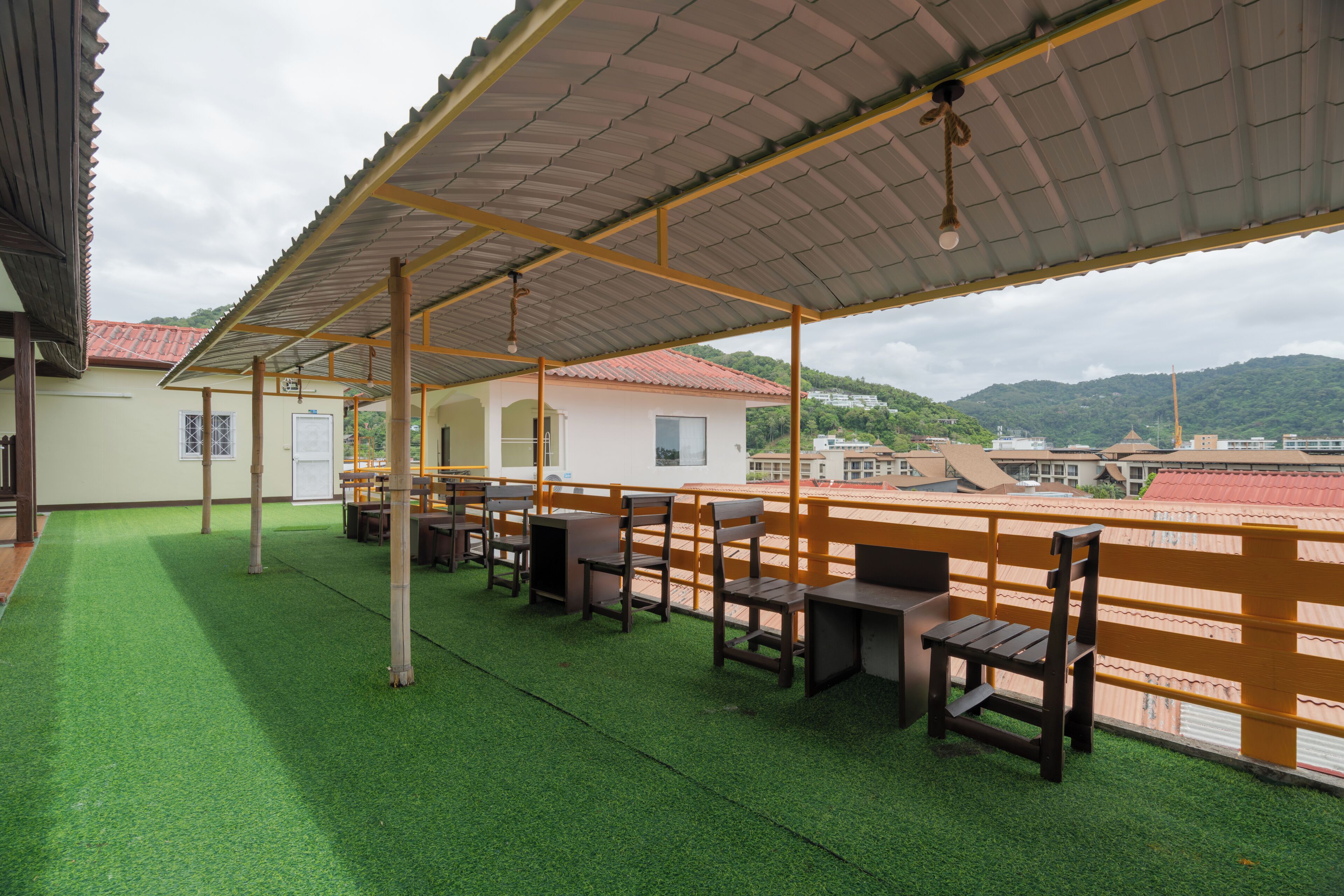 Une terrasse extérieure dotée d’une pelouse artificielle verte, de meubles en bois et d’une structure de toit en métal.