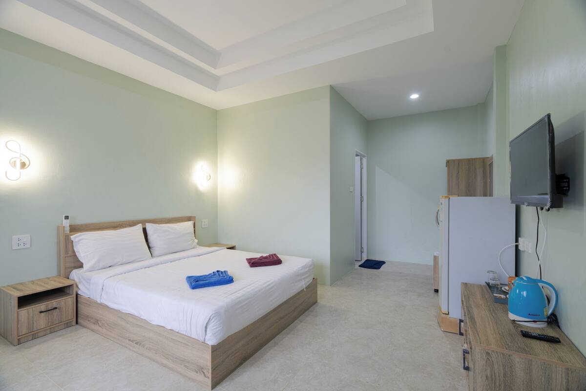 A hotel room with a bed, bedside tables, a TV, a refrigerator, and a kettle.