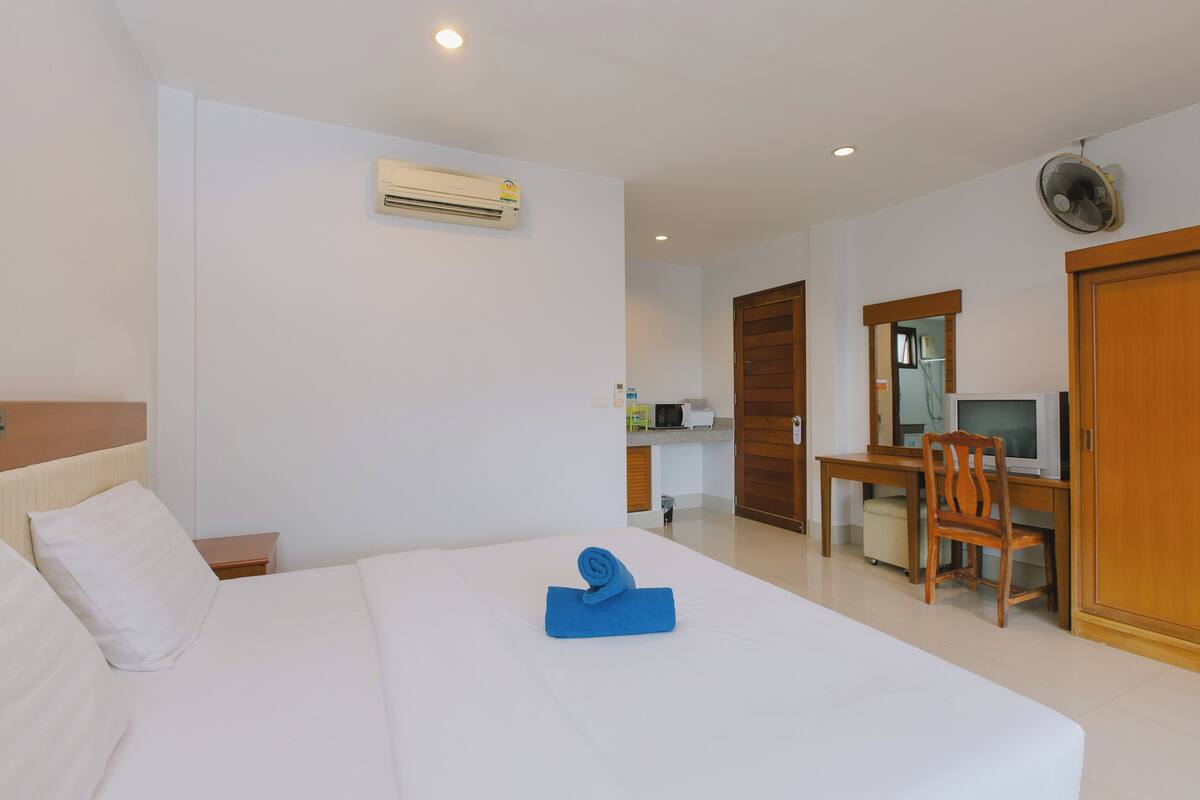 A hotel room with a bed, a desk with a chair, a television, and an air conditioning unit.