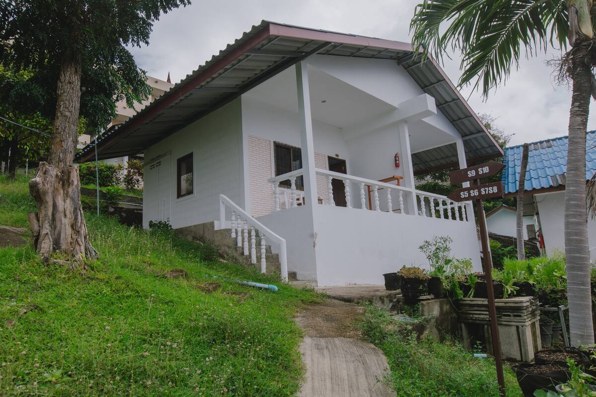 A white house with a porch and a staircase leading to the entrance. There are signs indicating prices for rooms or services.