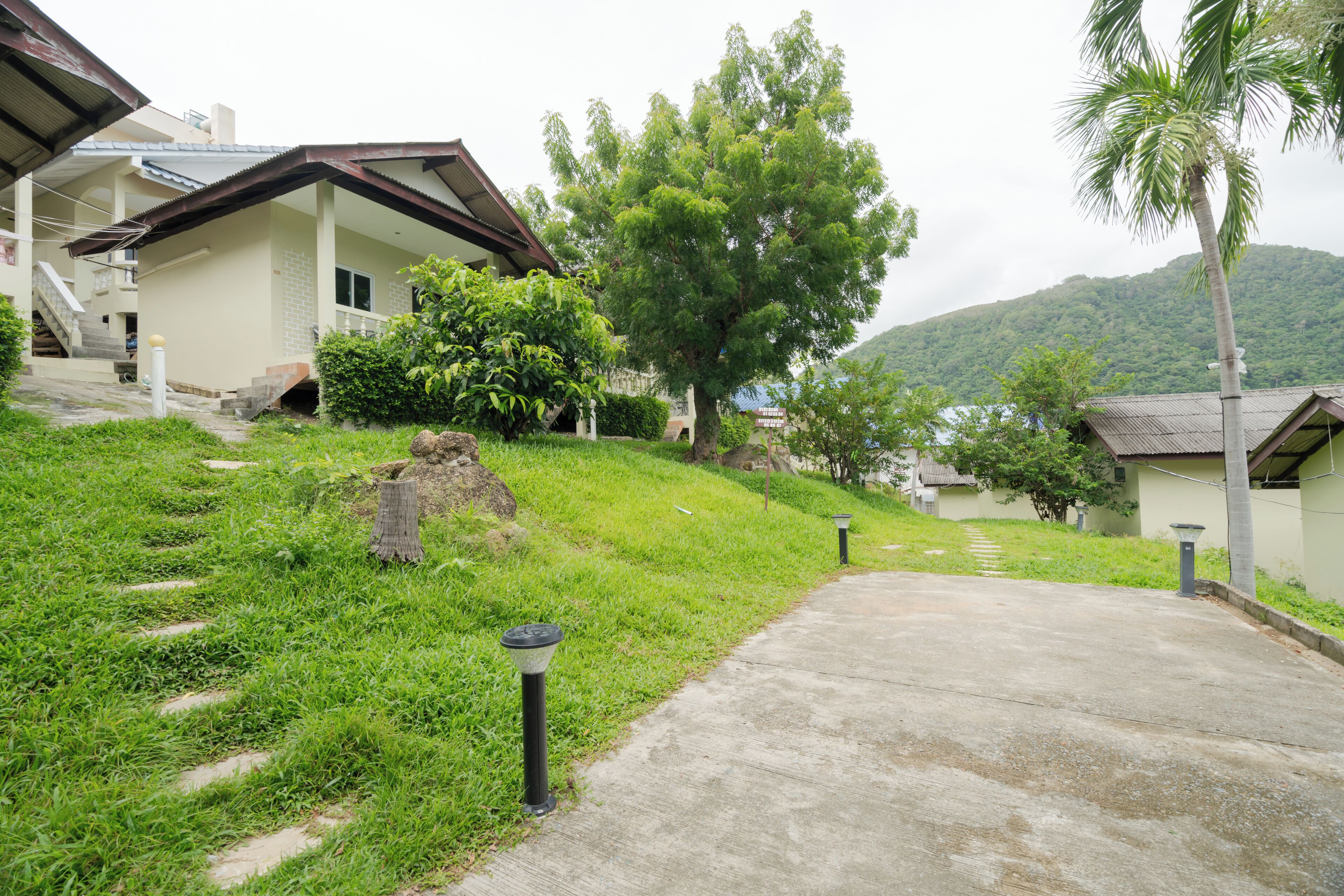 A residential area with houses, a concrete pathway, and a hillside.