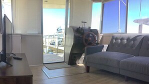 A living room with a grey sofa, a television on a wooden stand, and a large window with blinds. - Wake up on the Lake! … Gate Keeper (Port Clinton)