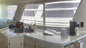 A kitchen with a sink, a window with blinds, and various kitchen items on the counter. - Wake up on the Lake! … Gate Keeper (Port Clinton)