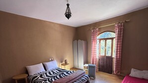Une chambre à coucher comprenant un lit, une petite table, un radiateur, une fenêtre avec des rideaux et un luminaire suspendu.