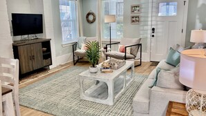 A living room with a TV, sofa, coffee table, and a plant. - The Entire Coastal Blue Bliss with heated POOL (Fernandina Beach)