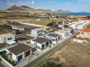 A residential area with modern houses, a main road, and a view of the sea and mountains in the background. - Quality villa, easy distance to beach|Vila Diana (Cabeco Da Ponta)