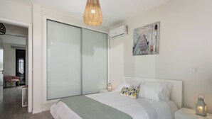 Une chambre à coucher comprenant un lit, une table de chevet, un climatiseur fixé au mur et un tableau.