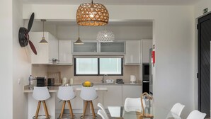 Une cuisine moderne avec des meubles blancs, une table à manger en verre et deux tabourets de bar.