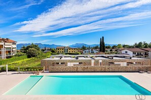 A swimming pool with a stone wall and a view of houses and mountains in the background. - Warda C11 Apartment by Wonderful Italy (Desenzano del Garda)