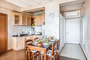A kitchen with wooden cabinets, a dining table set for four, and a clock on the wall. - Warda C11 Apartment by Wonderful Italy (Desenzano del Garda)