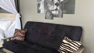 Un canapé noir avec deux coussins, un ciel de lit blanc et un mur orné de trois images de lions.