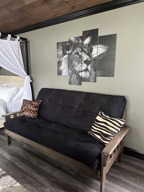 Un canapé noir avec deux coussins, un ciel de lit blanc et un mur orné de trois images de lions.