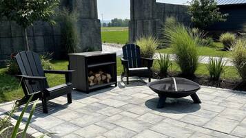 Eine Terrasse im Freien mit Feuerstelle, zwei Adirondack-Stühlen, einer Holzbank und einem Kamin aus Stein.