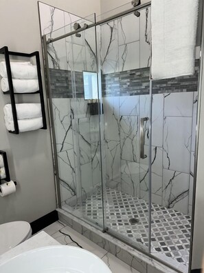 A modern bathroom with a glass-enclosed shower, marble walls, a tiled floor, and a toilet.