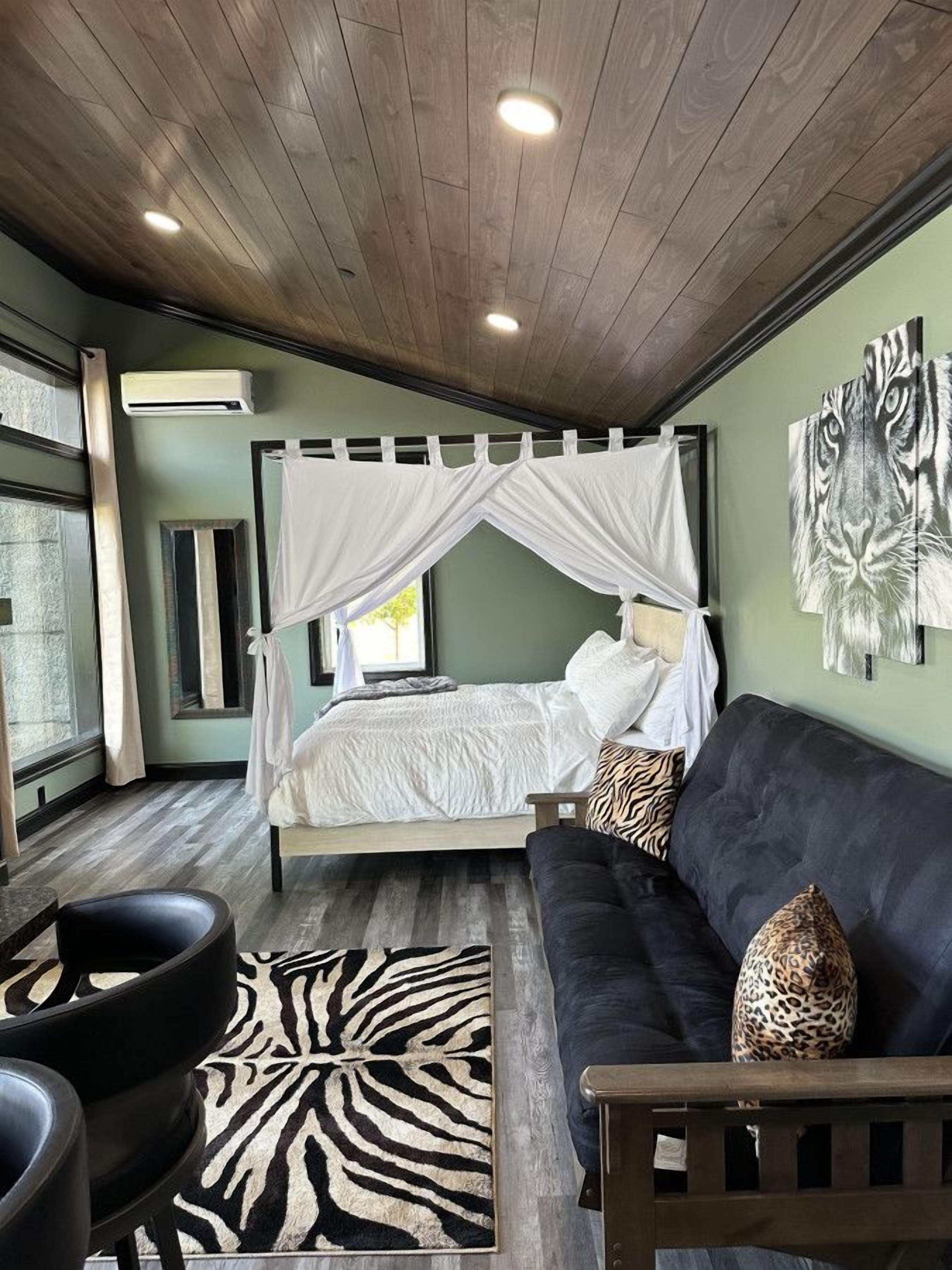 Une chambre à coucher avec un lit à baldaquin, un tapis à motifs zébrés, un canapé foncé et un banc en bois.
