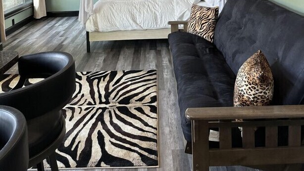 A bedroom with a four-poster bed, a zebra-patterned rug, a dark sofa, and a wooden bench.
