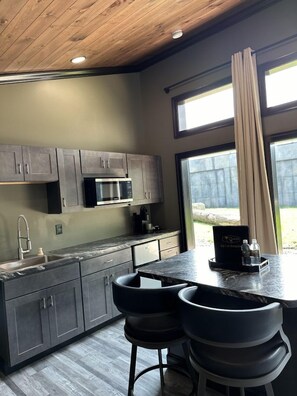 A modern kitchen with dark cabinets, a built-in microwave, a sink, and a bar area with stools.