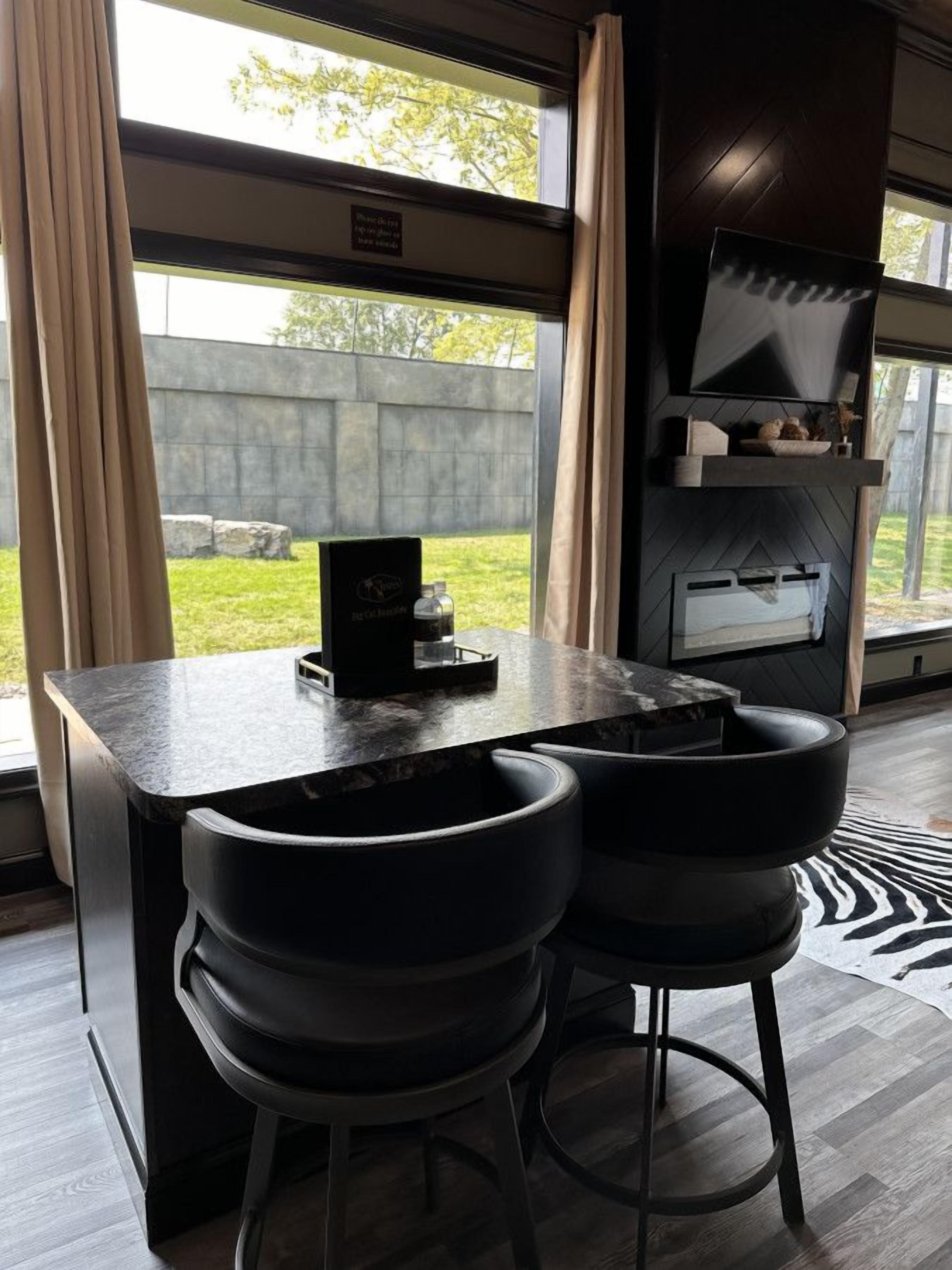 A modern kitchen with a built-in grill, two bar stools, and a view of the outdoors.