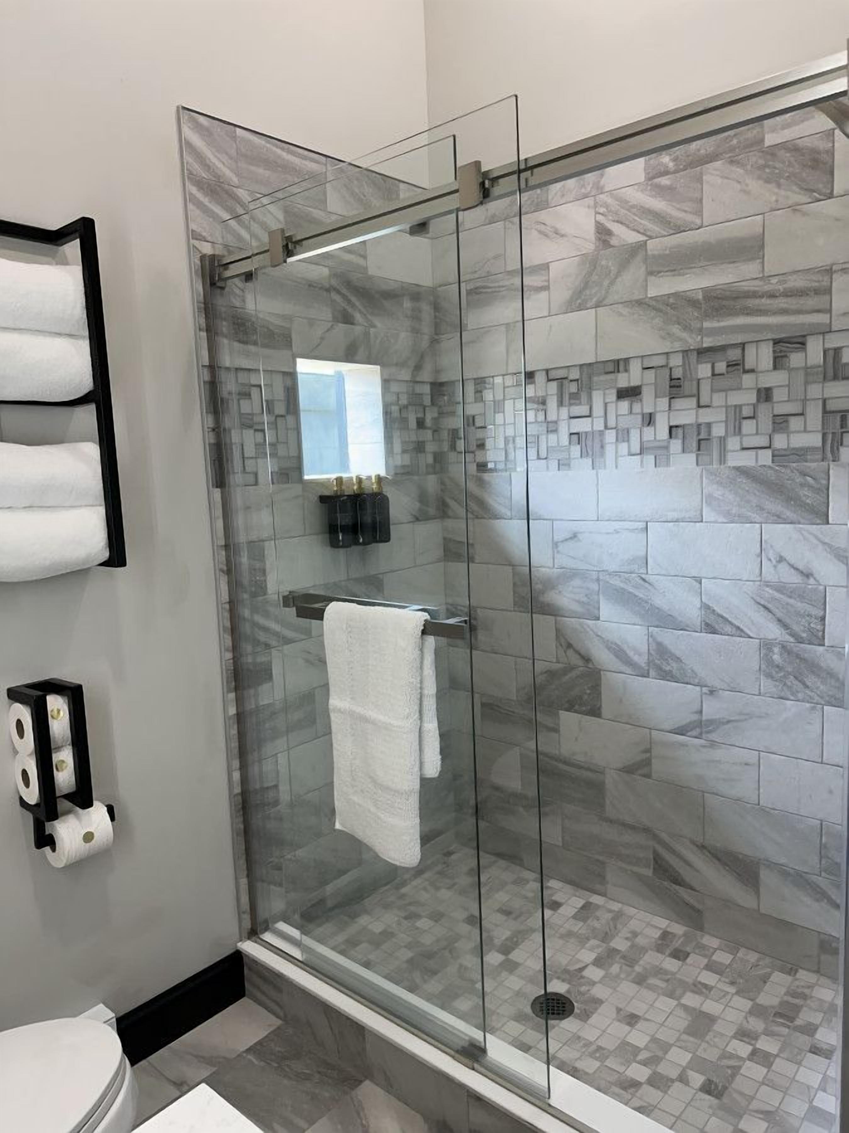 A modern bathroom with a glass-enclosed shower, marble tiles, a towel rack, and a toilet.