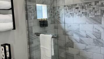 A modern bathroom with a glass-enclosed shower, marble tiles, a towel rack, and a toilet.