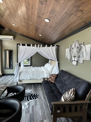 A bedroom with a canopy bed, a zebra-patterned rug, a black leather sofa, and a lion artwork on the wall.