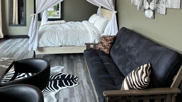A bedroom with a canopy bed, a zebra-patterned rug, a black leather sofa, and a lion artwork on the wall.