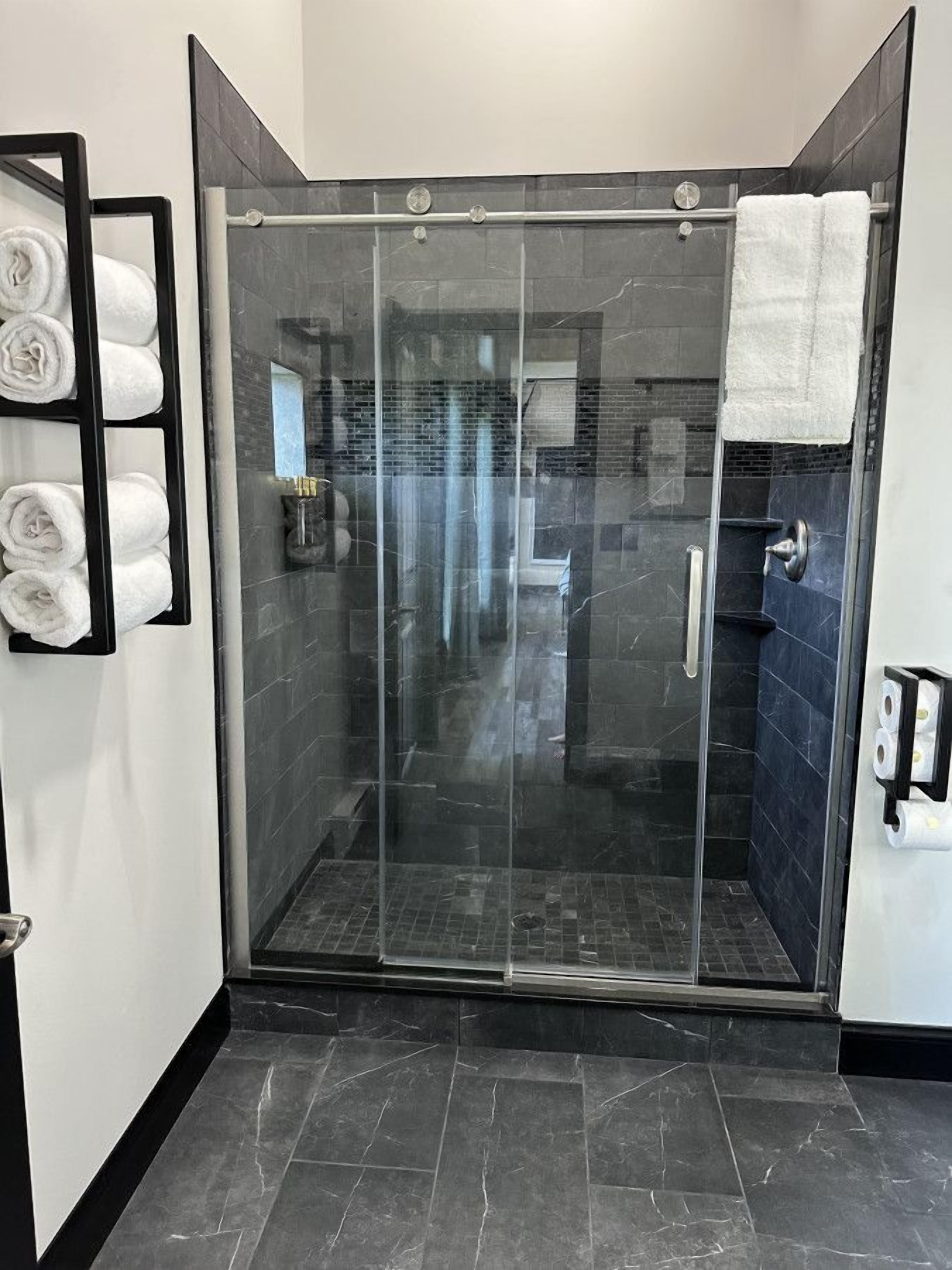 A modern shower area with a glass door, dark tiled walls, and a black floor.