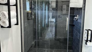 A modern shower area with a glass door, dark tiled walls, and a black floor.