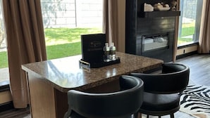 A bar area with a granite countertop, two black bar stools, and a television mounted on the wall.