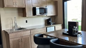 A modern kitchen with wooden cabinets, a built-in microwave, a sink, and a bar area with stools.