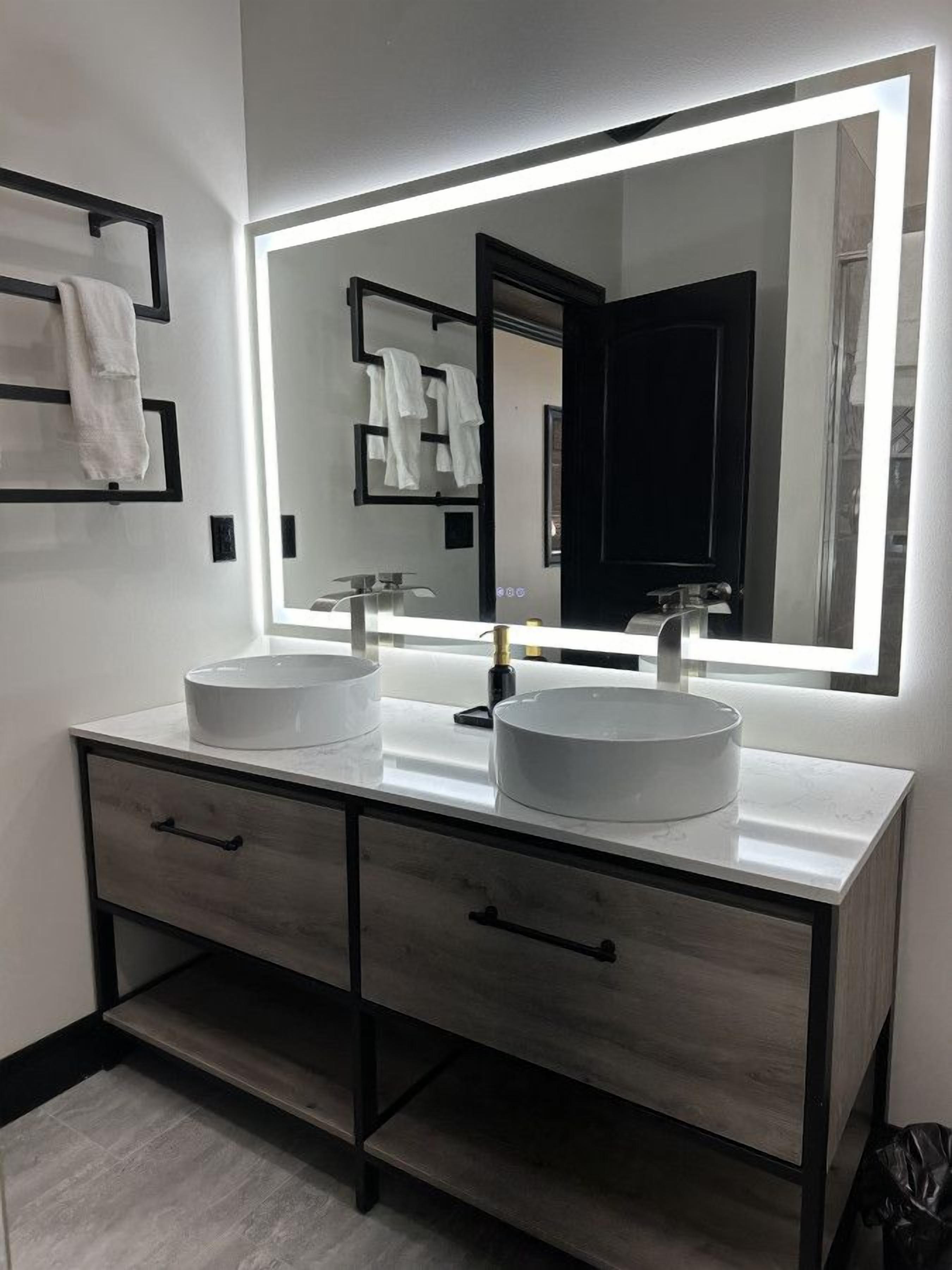 Une salle de bain moderne avec deux vasques, un grand miroir et un meuble-lavabo aux tons foncés doté de tiroirs.