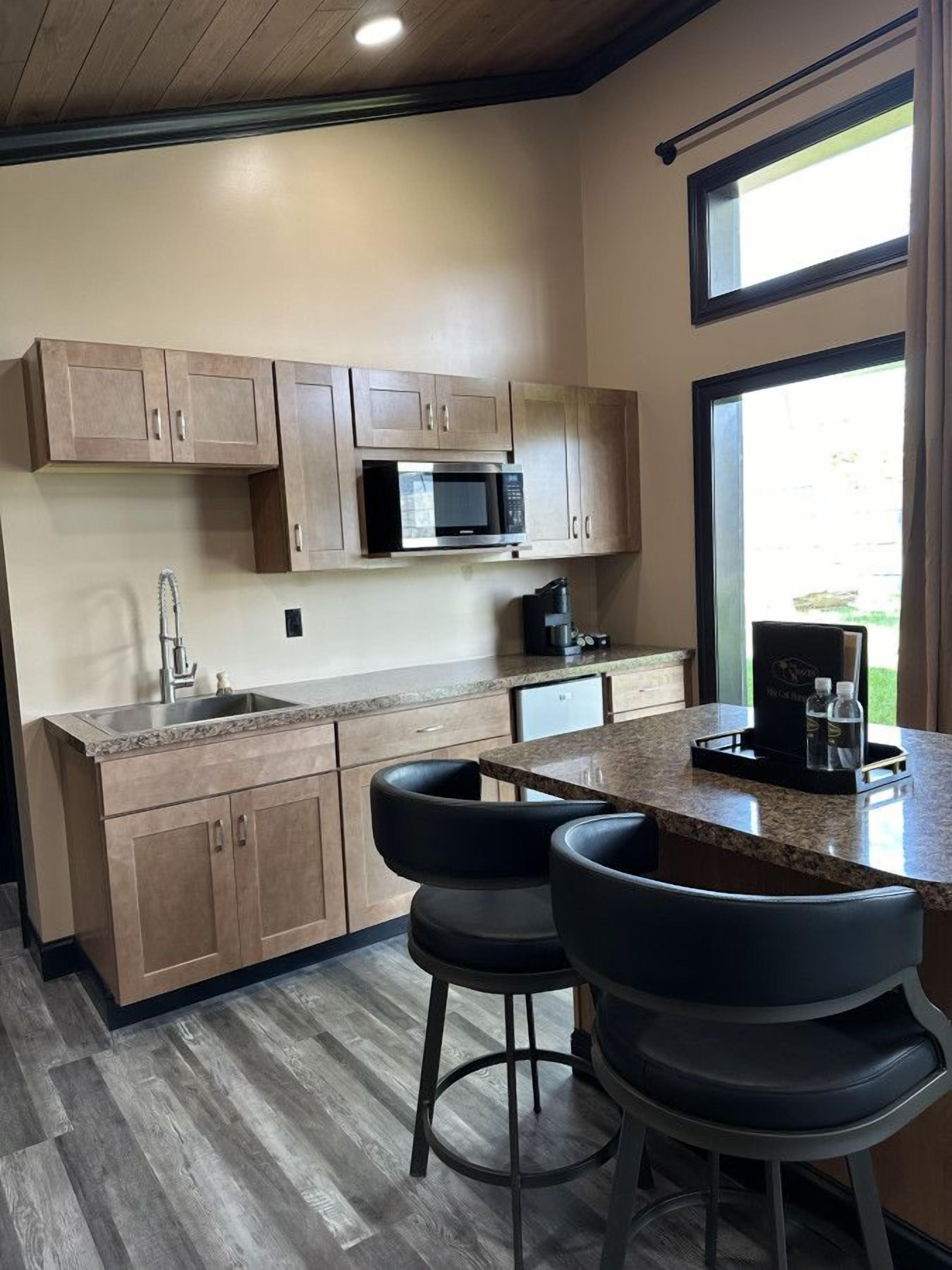 A modern kitchen with wooden cabinets, a built-in microwave, a sink, and a bar area with stools.