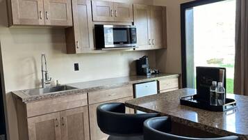 A modern kitchen with wooden cabinets, a built-in microwave, a sink, and a bar area with stools.